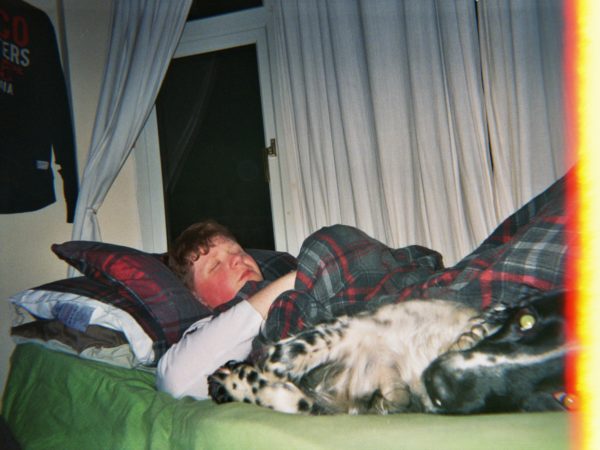 Fred's photograph (for the 21st Century Kids) of his brother asleep in bed. There is a dog also on the bed looking a the camera in the foreground.
