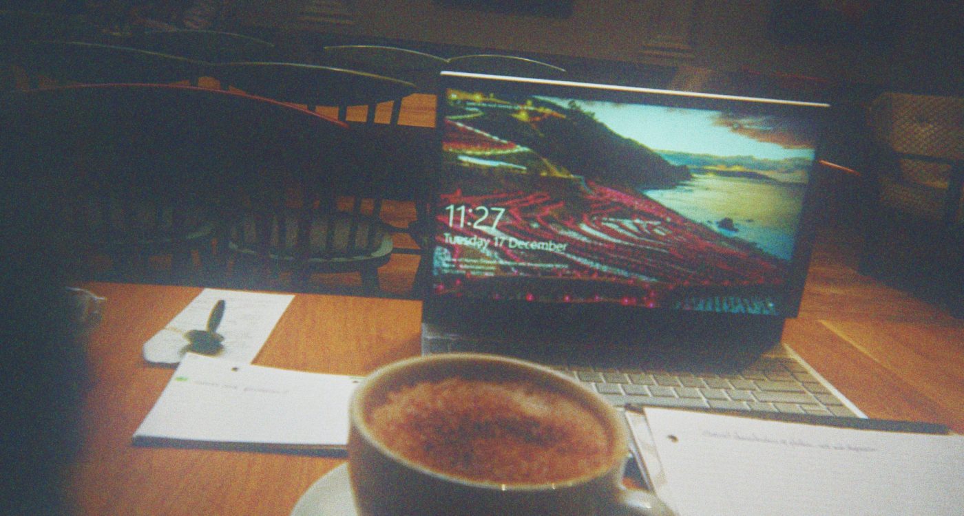 Lydia's photograph (for the 21st Century Kids) of table in coffee shop with open laptop, cup of what looks like coffee or hot chocolate and paper with notes