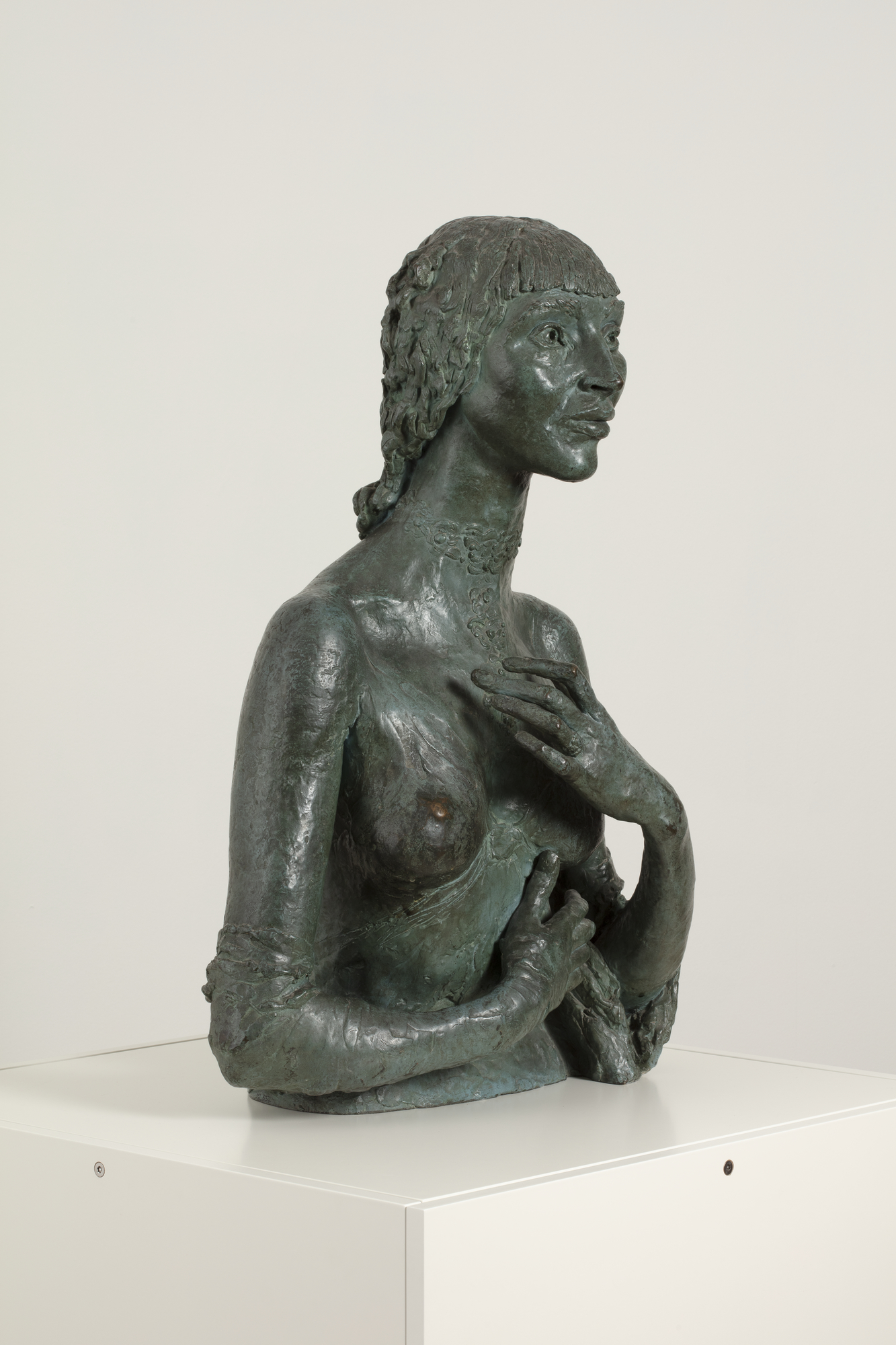 A bronze sculpture of a smiling naked woman shown from the waist up, with hands raised, one across her stomach and the other in front of her left breast.