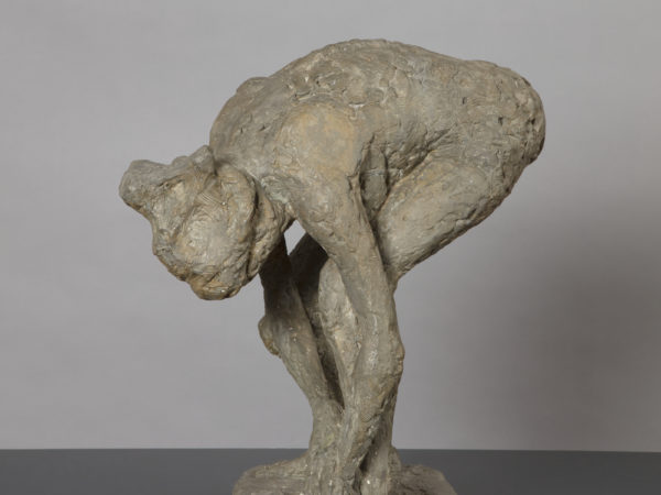 A sculpture of a naked woman bending forward drying her left foot with a towel that is held in both hands