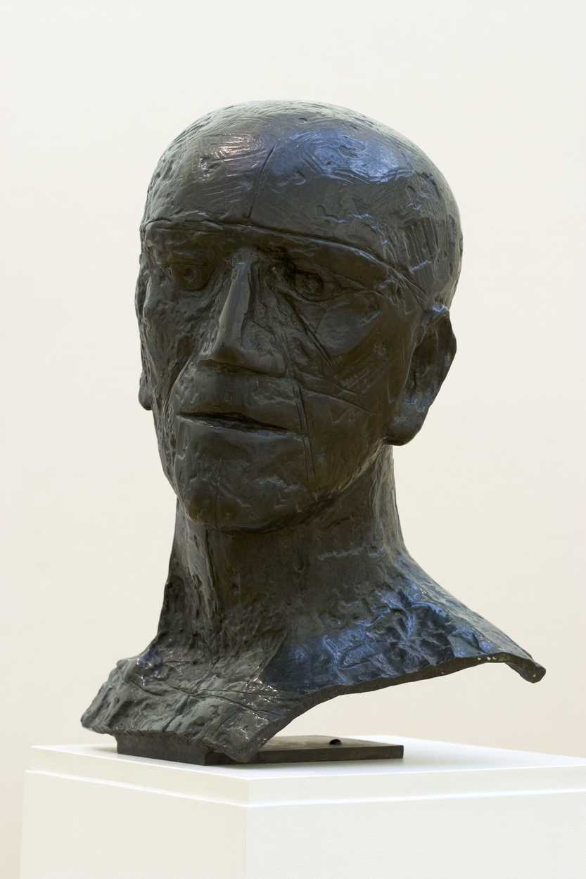 Bronze sculpture of the head and neck of a bald-headed man facing foward. His wide mouth is thin-lipped and his eyes appear to stare into the distance.
