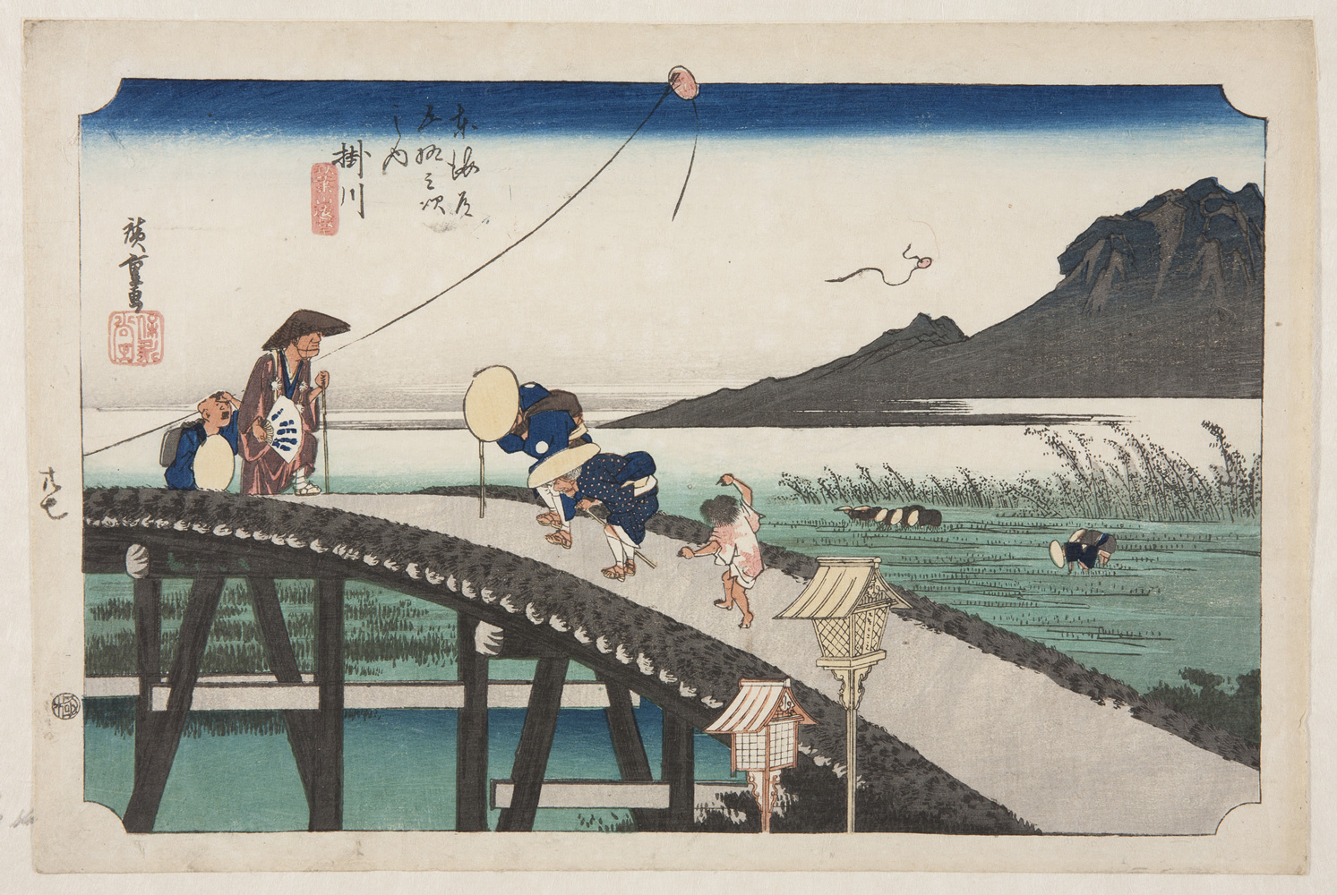 japanese print of people in traditional japanese dress walking over a wooden brige. in the background people pick rice in rice fields in front of a mountain