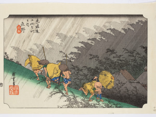 Japanese print. Travelers walk along a hillside dressed in traditional clothes. Two carry a passenger on a chair. They are bent against the weather and the rain slants across the scene top right to bottom left.