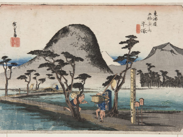 japanese print of a road zig-zagging through a marshy area. on the road a delivery man carrying a box on his back runs past two walking travellers