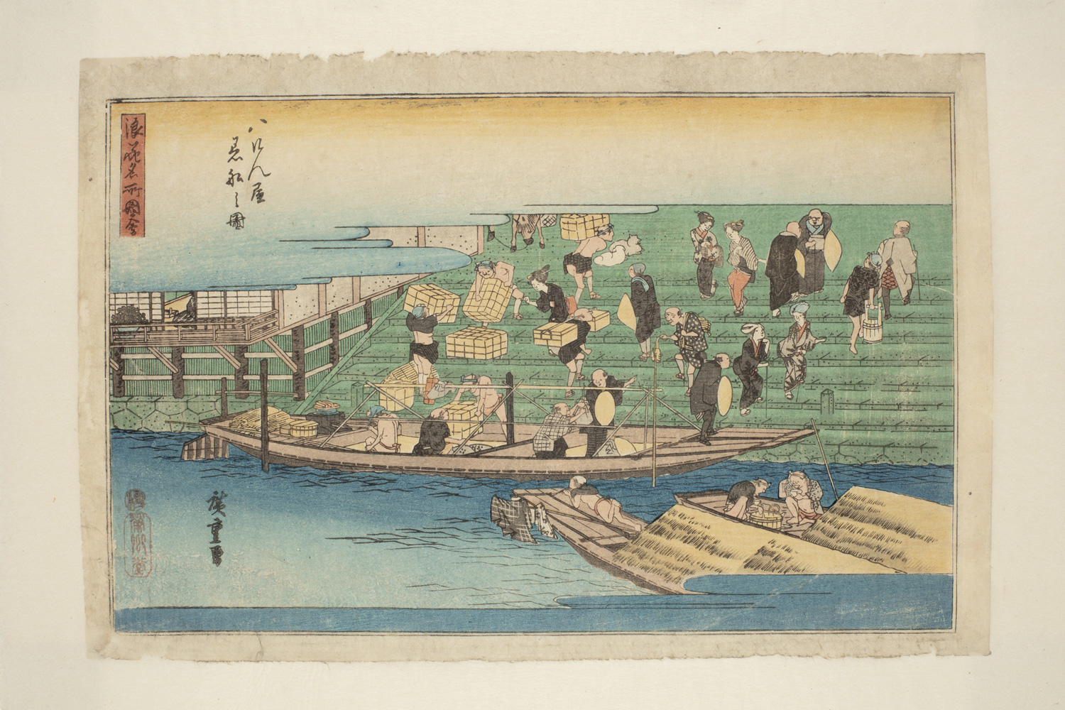 Japanese print of a harbour scene. A boat is moored at the quay and men are unloading it and carrying bundles of cargo up the steps behind.