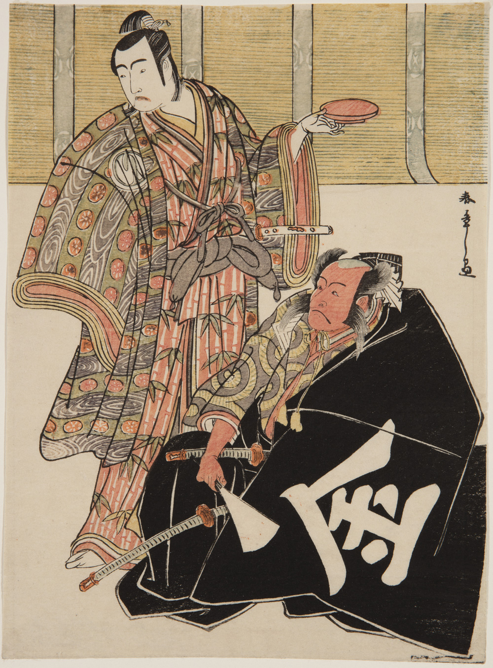 A Japanese print of two actors dressed in traditional robes. One is seated and is draped in a black cloak, holding a fan, two swords are visible. The other stands behind him and is holding a dish.