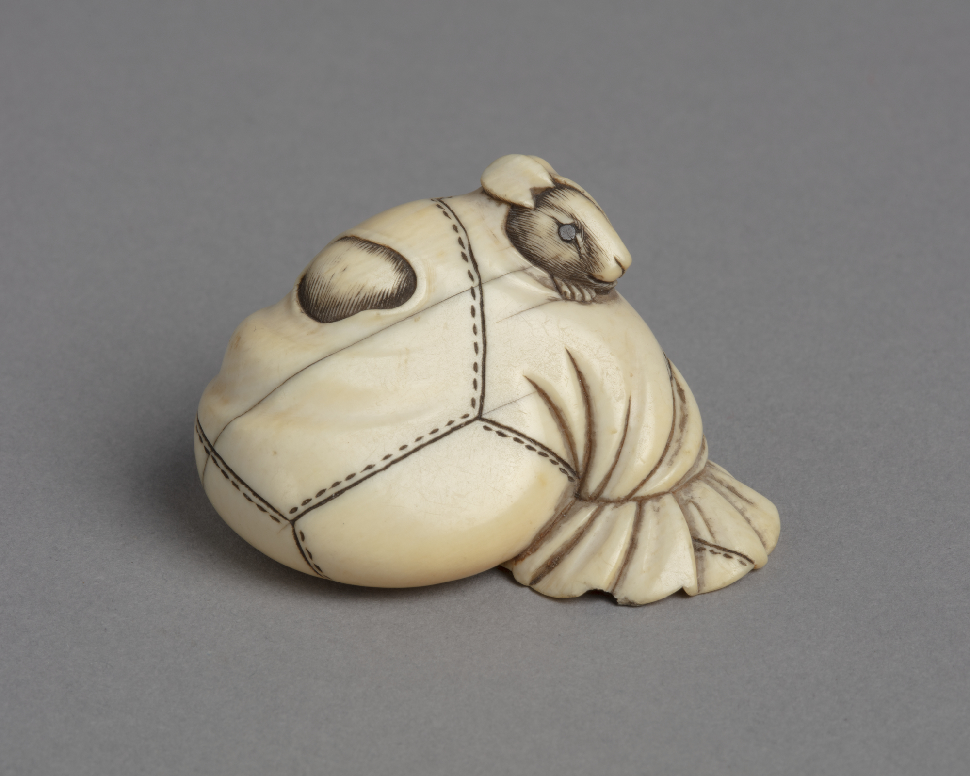 A Japanese ivory netsuke of a rat poking its head through a hole in a stitched rice-bag.