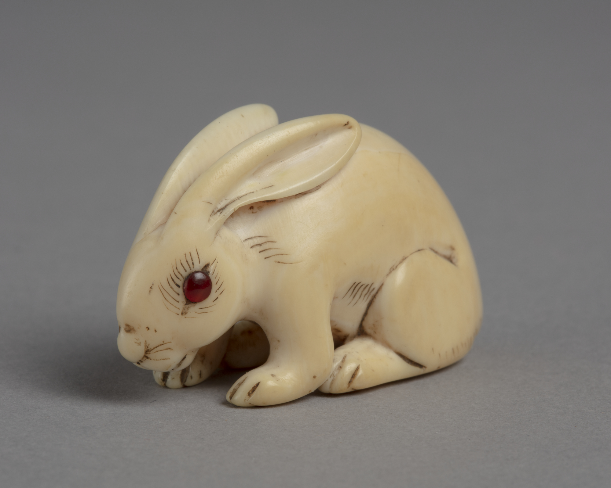 A Japanese ivory of a netsuke of a crouched white rabbit. Eyes are inlay with red coral.