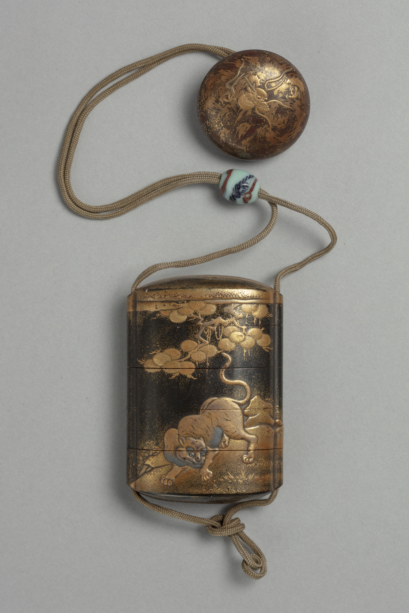 A Japanese black and gold lacquered five compartment inro box with dragon and tiger design, attached to a circular lacquer netsuke toggle.