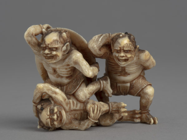 A Japanese ivory okimono ornament with three demons cowering and running away from the soybeans being thrown at them.