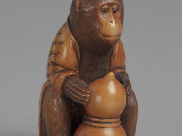 A Japanese boxwood netsuke of a monkey wearing a robe, seated and holding a double gourd in its paws.