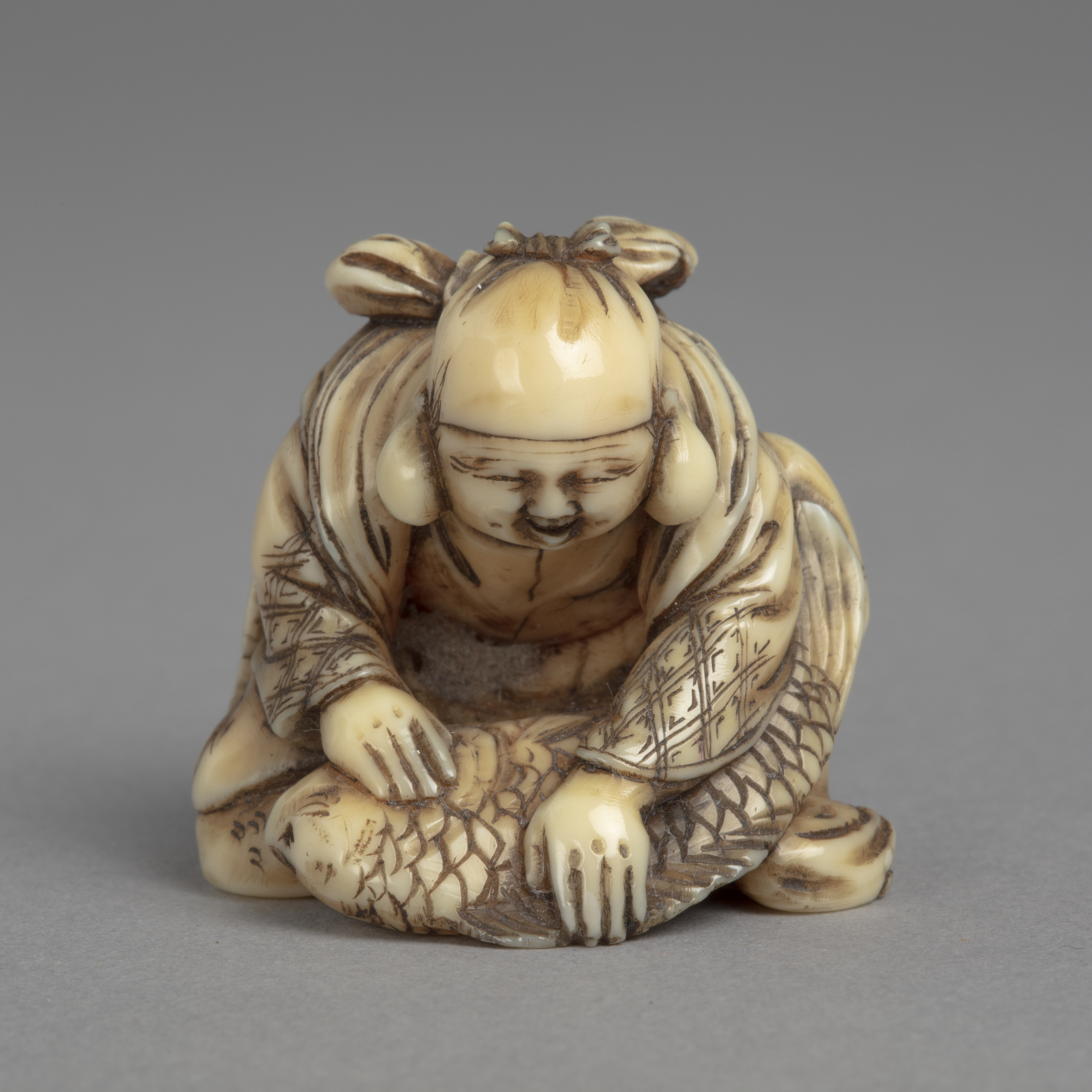 A Japanese ivory netsuke of Ebisu, one of the Seven Lucky Gods, kneeling over a large sea bream.