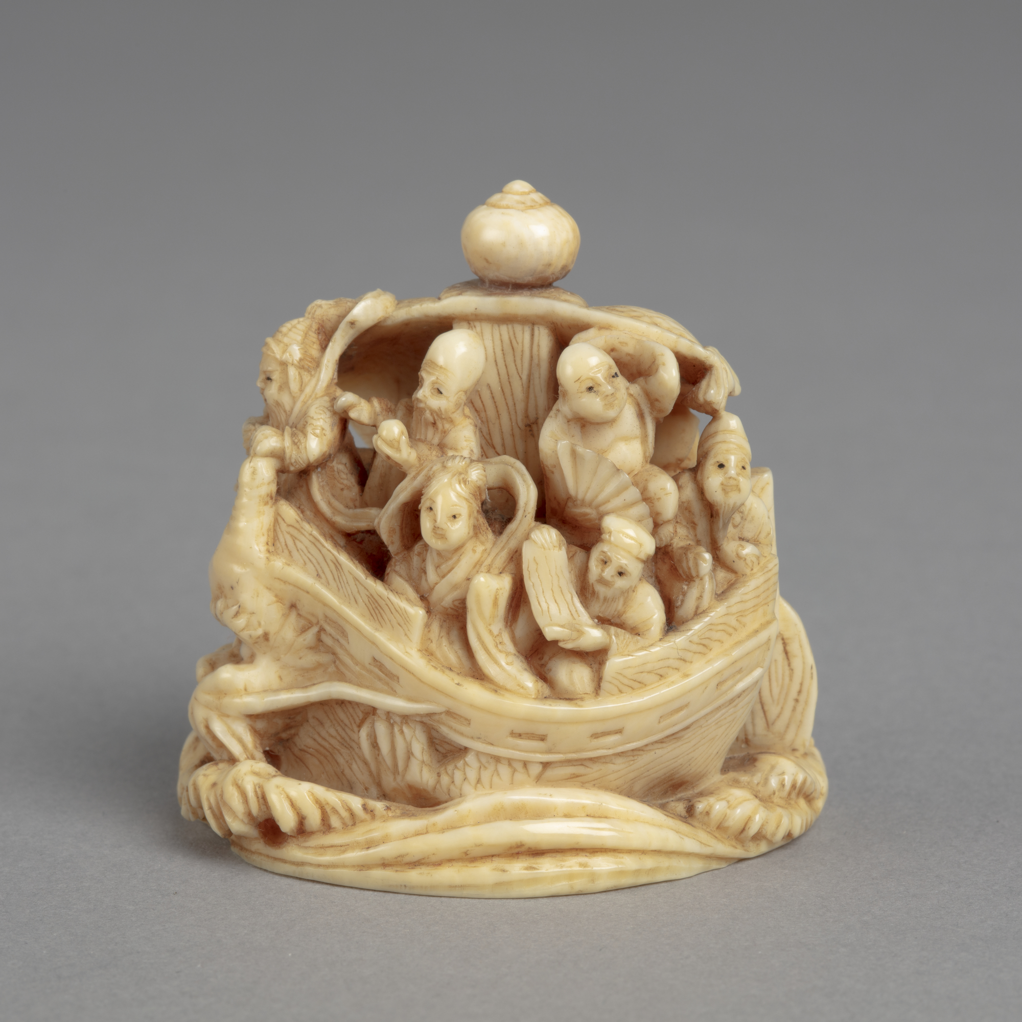 A Japanese ivory okimono ornament of the Seven lucky Gods aboard the Ship of Good Fortune which has the head of a dragon.