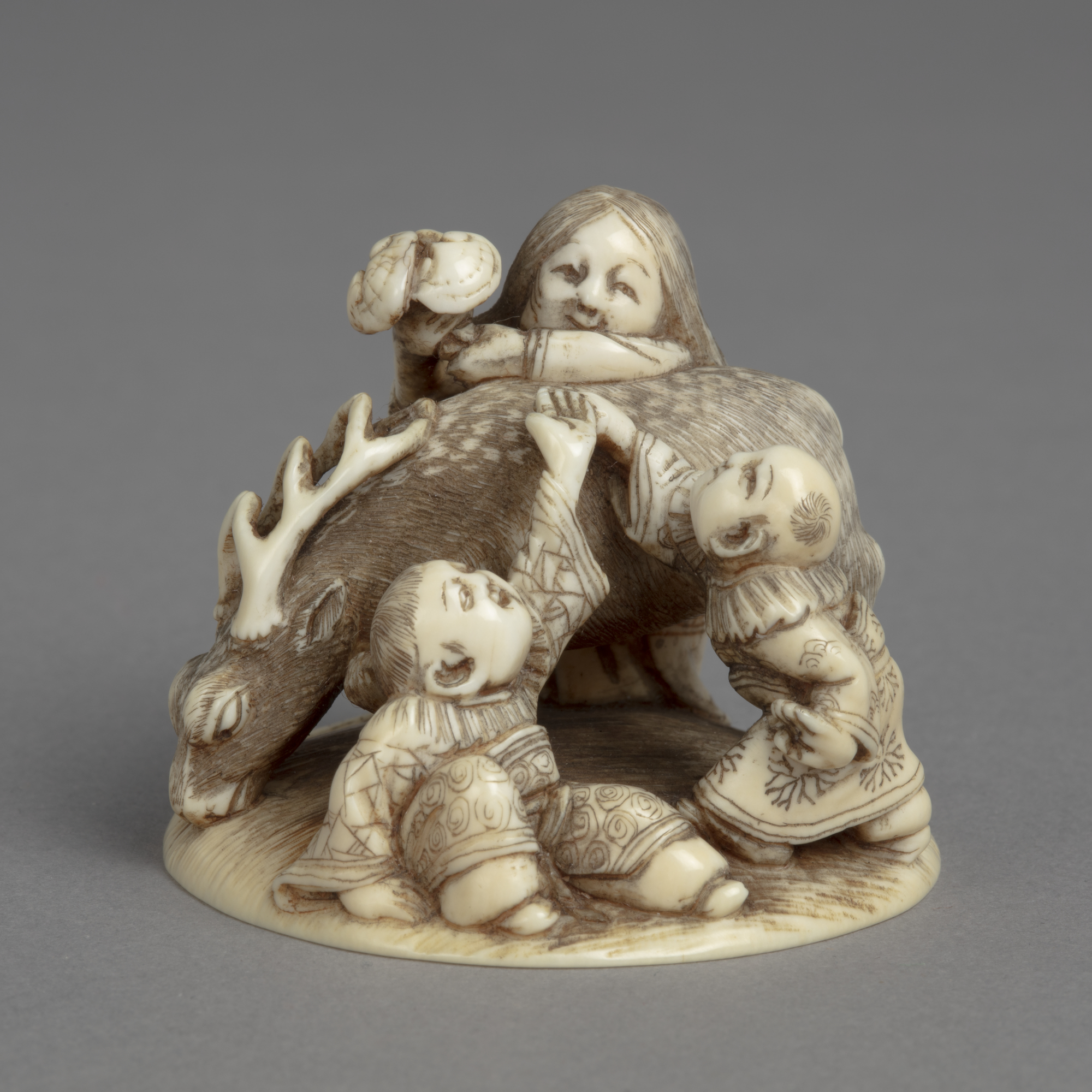 A Japanese ivory okimono ornament of a woman passing the Fungus of Immortality over a deer to two boys in Chinese dress.