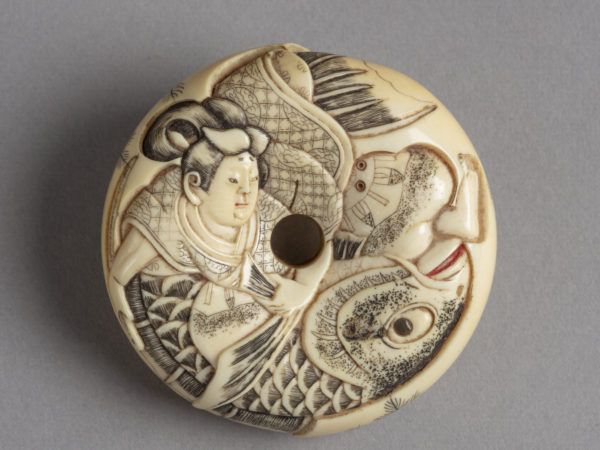 A Japanese ivory netsuke of a man fighting a very large fish carved on a doughnut-shaped disk.