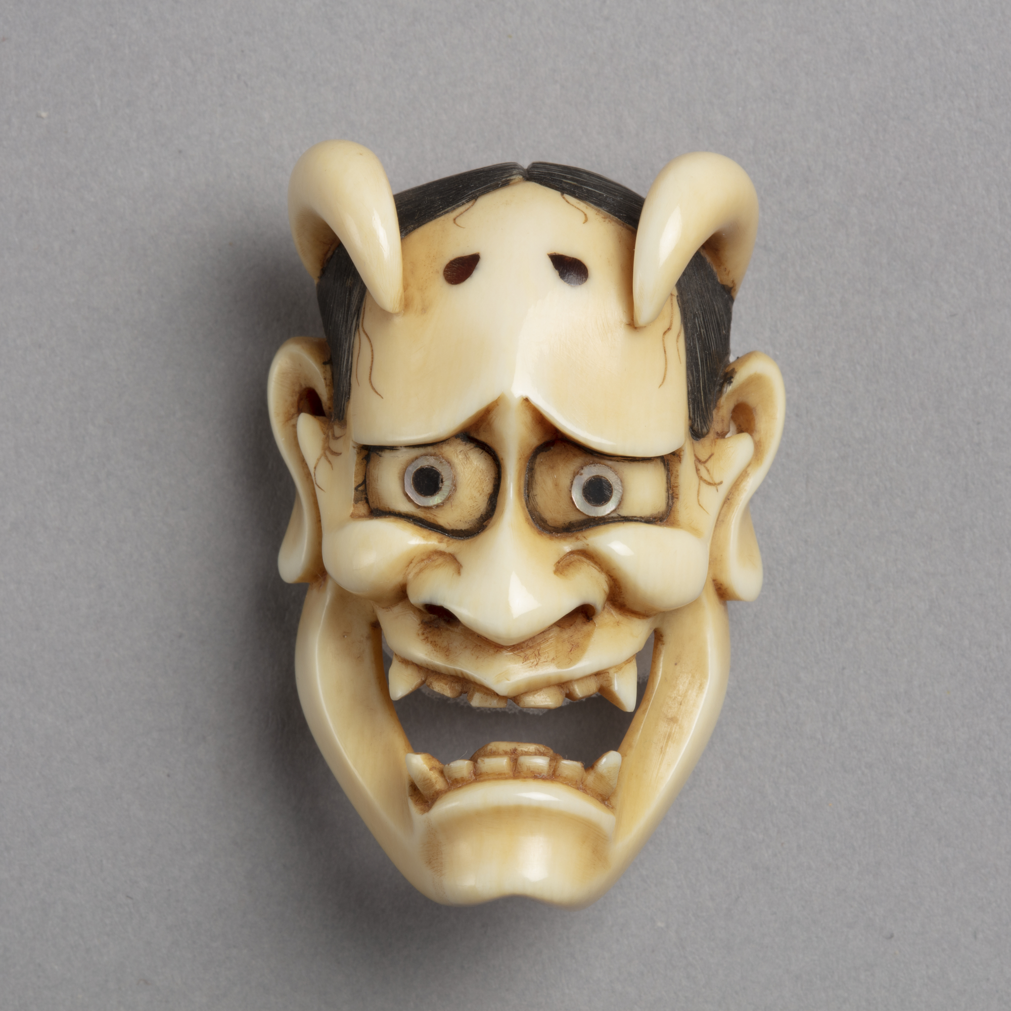 A Japanese ivory mask netsuke of Hannya the face of a jealous woman who took on the features of a demon including its horns.
