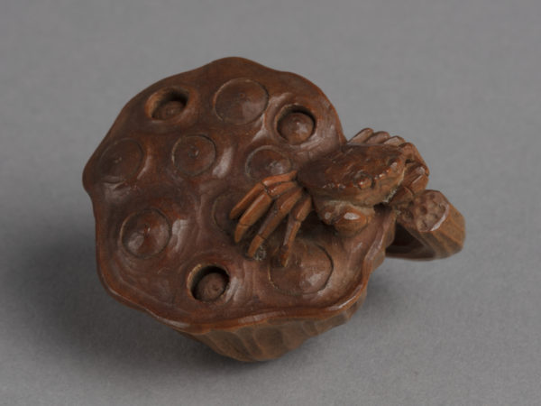 A Japanese boxwood netsuke of a small crab crawling across a lotus seedpod.