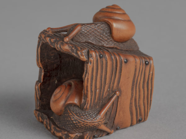 A Japanese boxwood netsuke of a pyriform wooden well bucket with one snail on top and one snail inside.