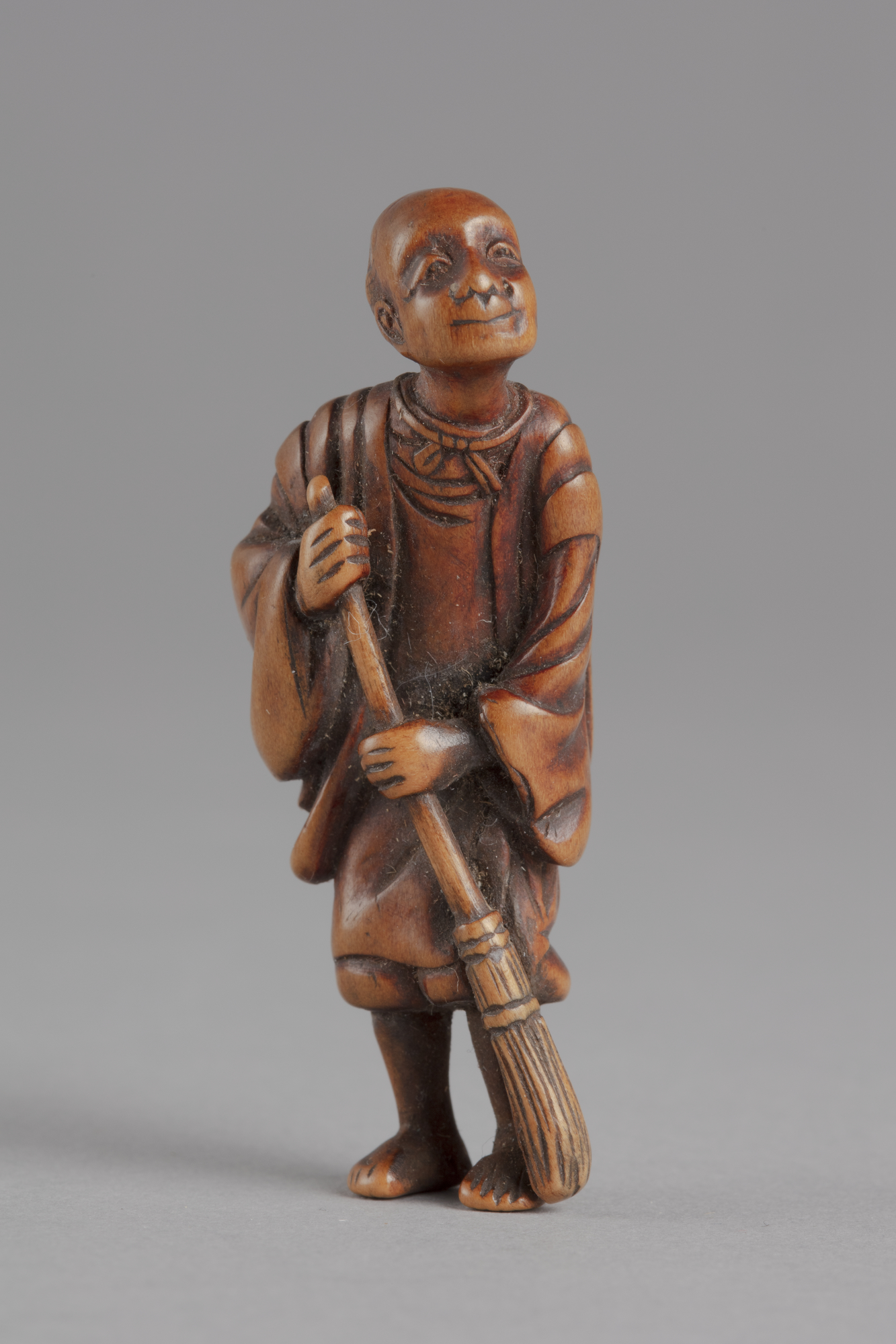 A Japanese boxwood netsuke of a robed elder with a broom sweeping the ground.