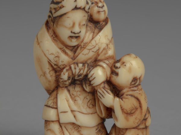 Japanese ivory netsuke of a standing mother in kimono and headscarf with a baby bundled on back and a boy to her left.