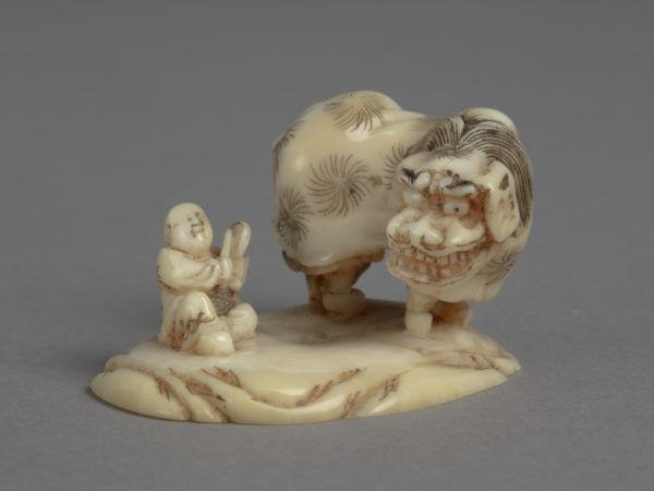 A Japanese ivory okimono ornament of two boys performing lion dance, another seated boy drumming.