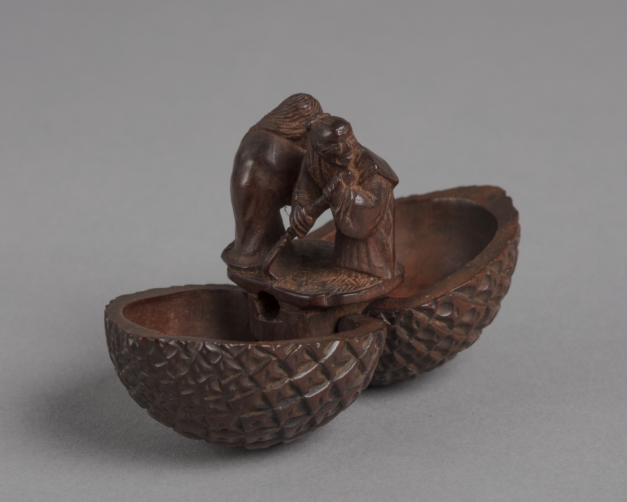 A Japanese boxwood netsuke of a pinecone which opens vertically to reveal a small man and woman standing inside.
