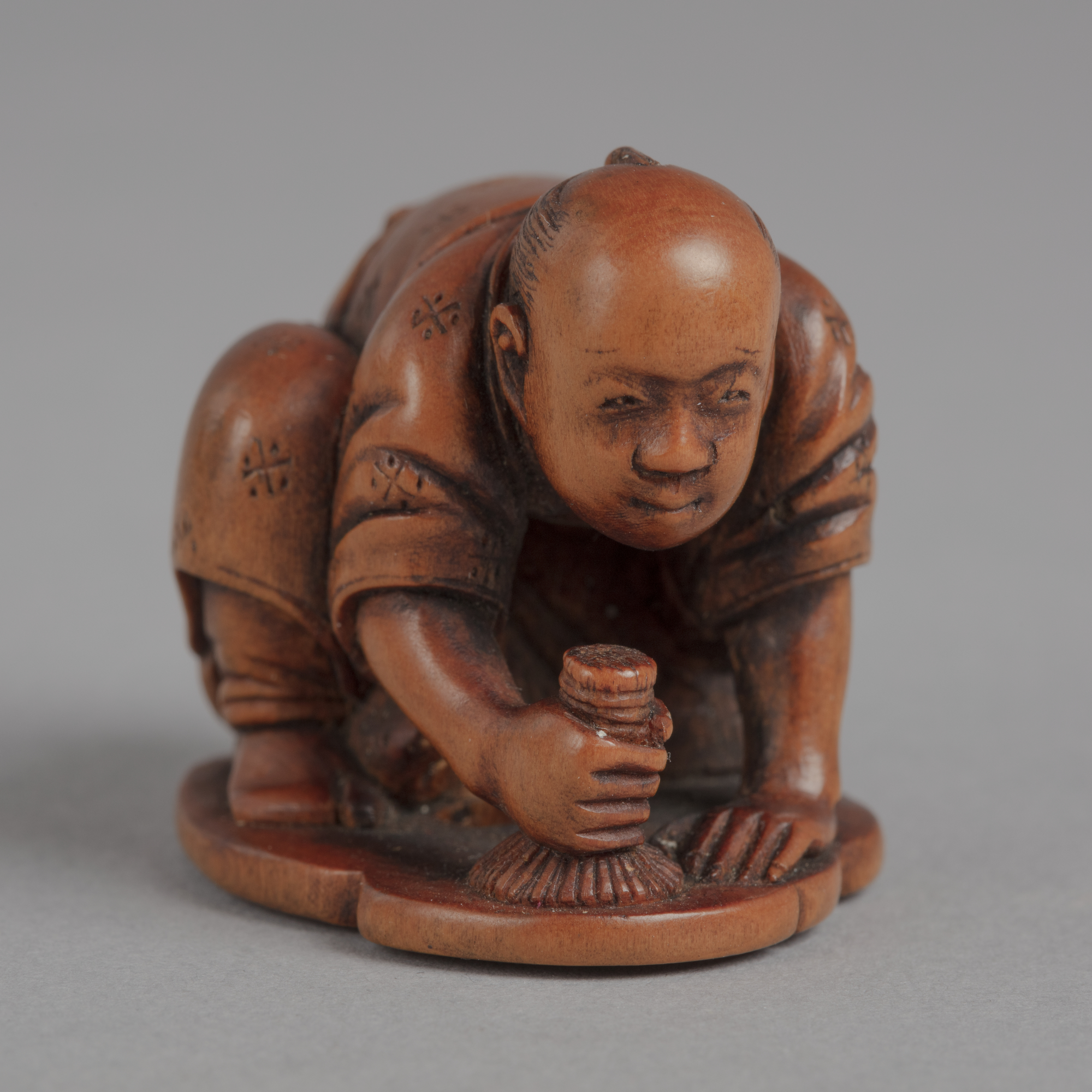 A Japanese boxwood netsuke of a man on his hands and knees polishing the floor with a brush, forming a swirling pattern.