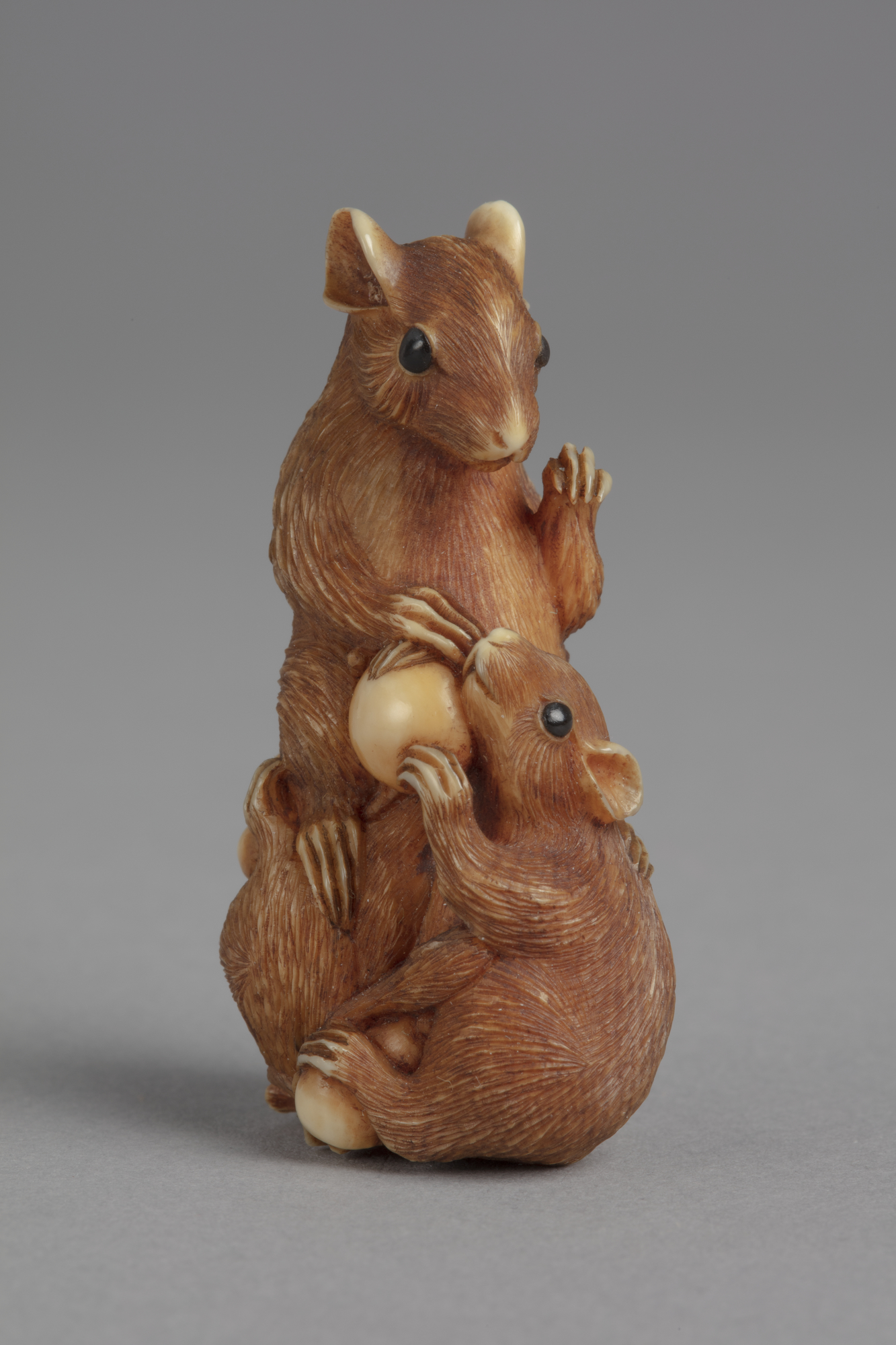 A Japanese ivory netsuke of a recumbent deer with its head turned back along the left side of its body. Eyes inlay with jet. 125 characters A Japanese netsuke of three rats with grapes. The central rat is bigger than the two by its feet.