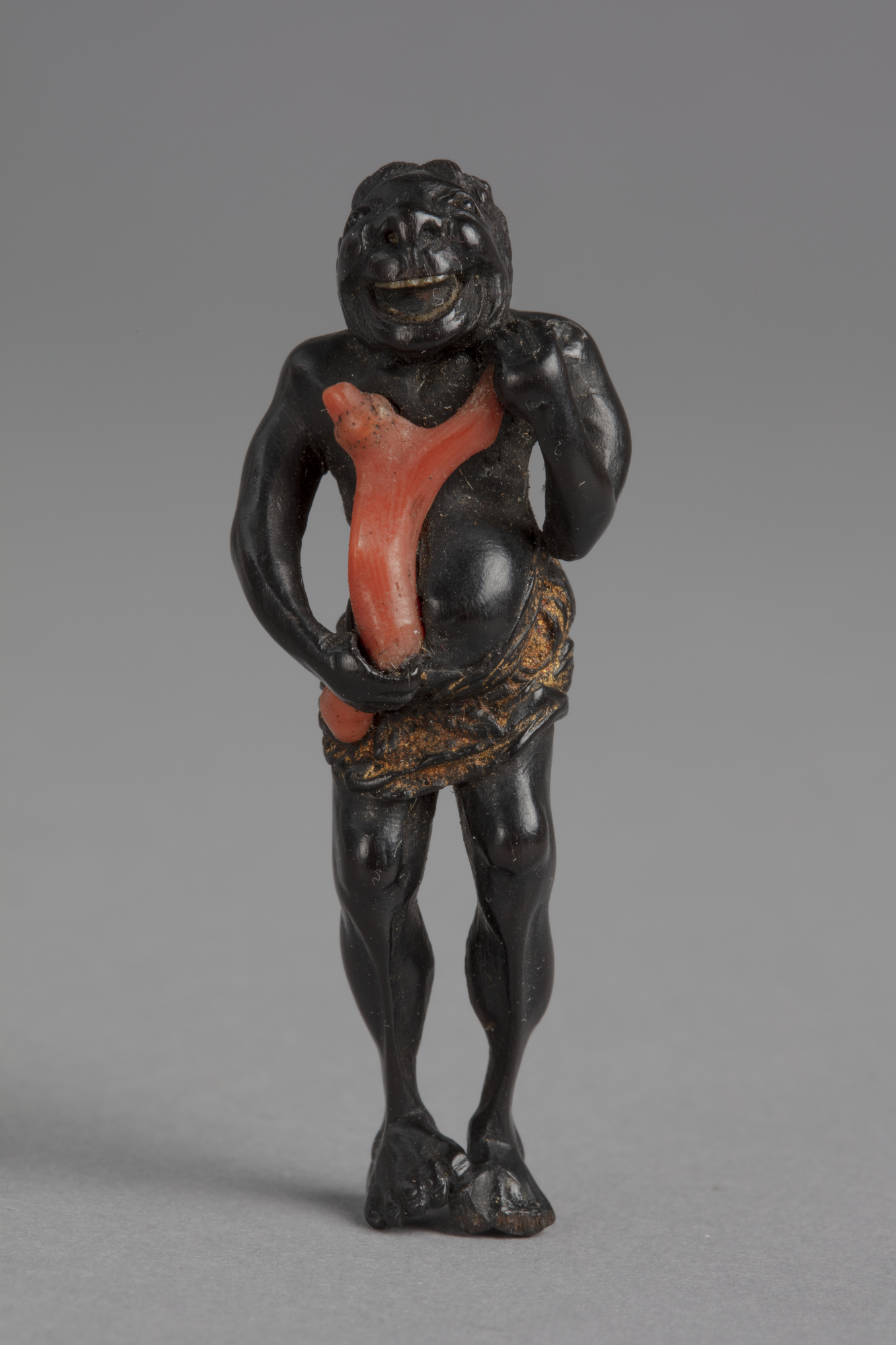 A Japanese ebony netsuke of a Black man wearing a gold loincloth holding a large branch of coral to his chest.
