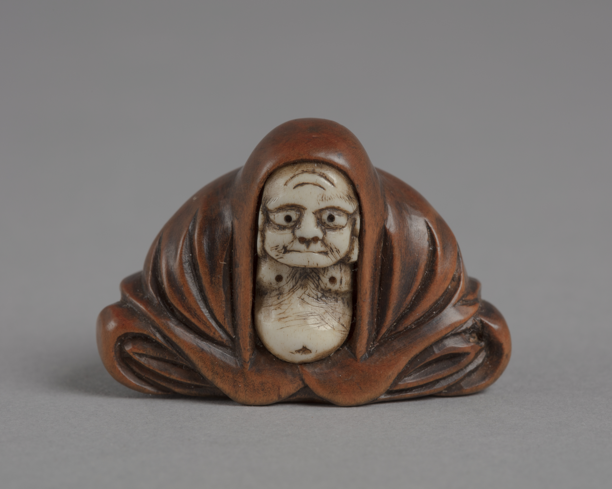 A Japanese boxwood and ivory netsuke of Daruma, a Zen priest seated with belly exposed and wearing a red robe.