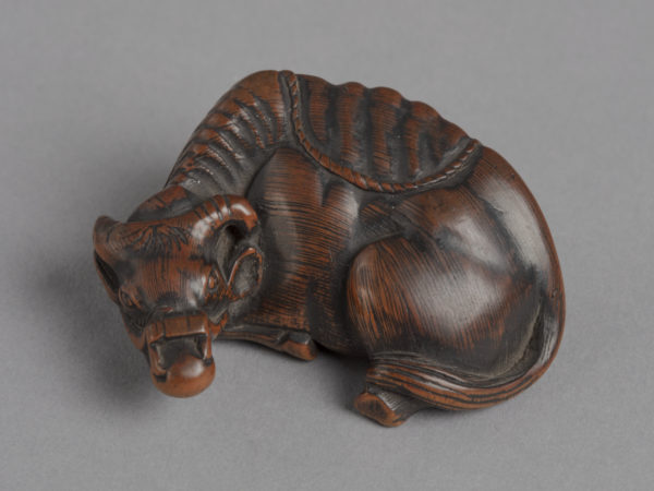 A Japanese boxwood netsuke of a recumbent ox with a bridle on its head.