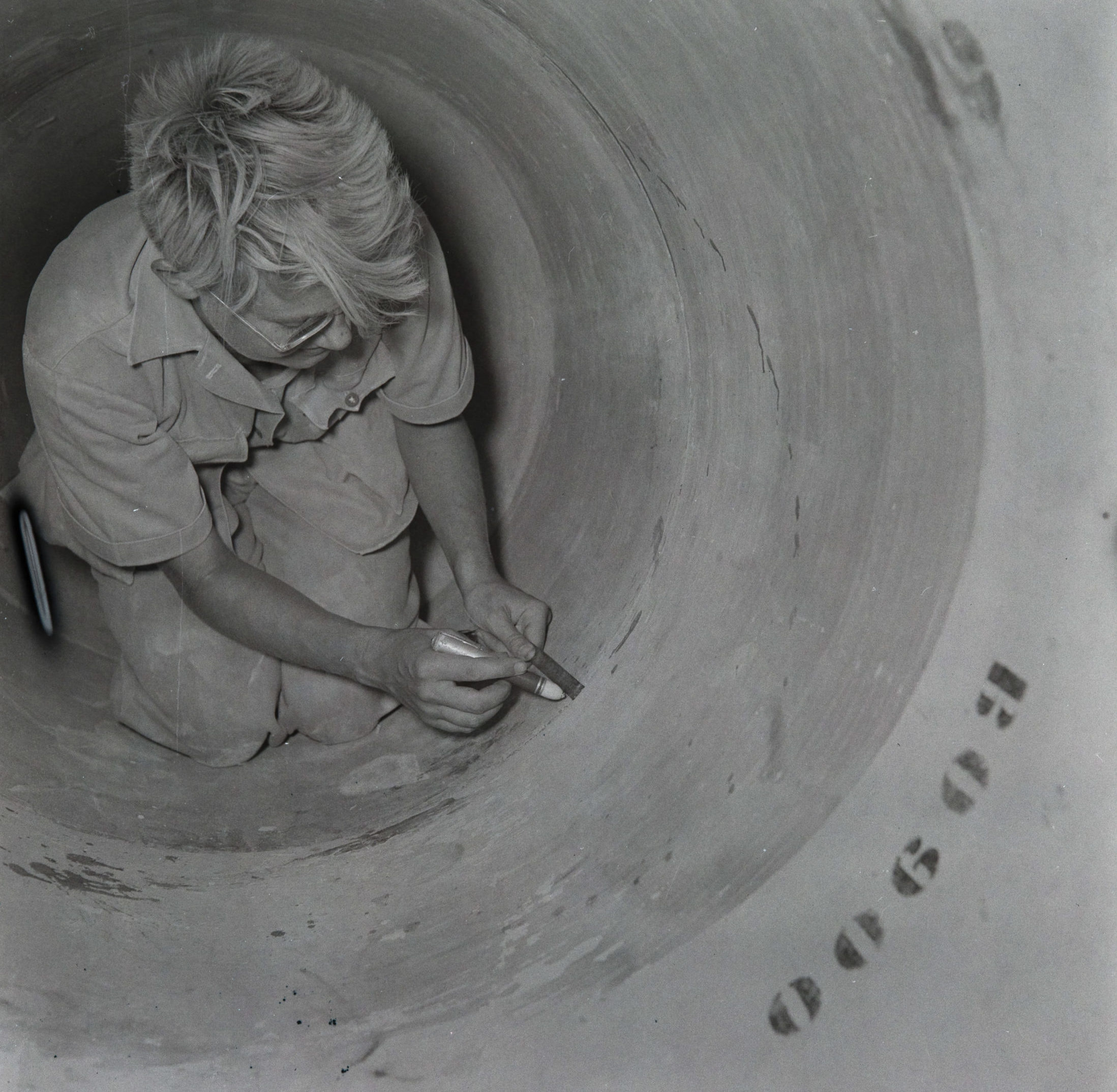 Black and white photo of Marie Lindley inspects a joint inside the water pipeline.
