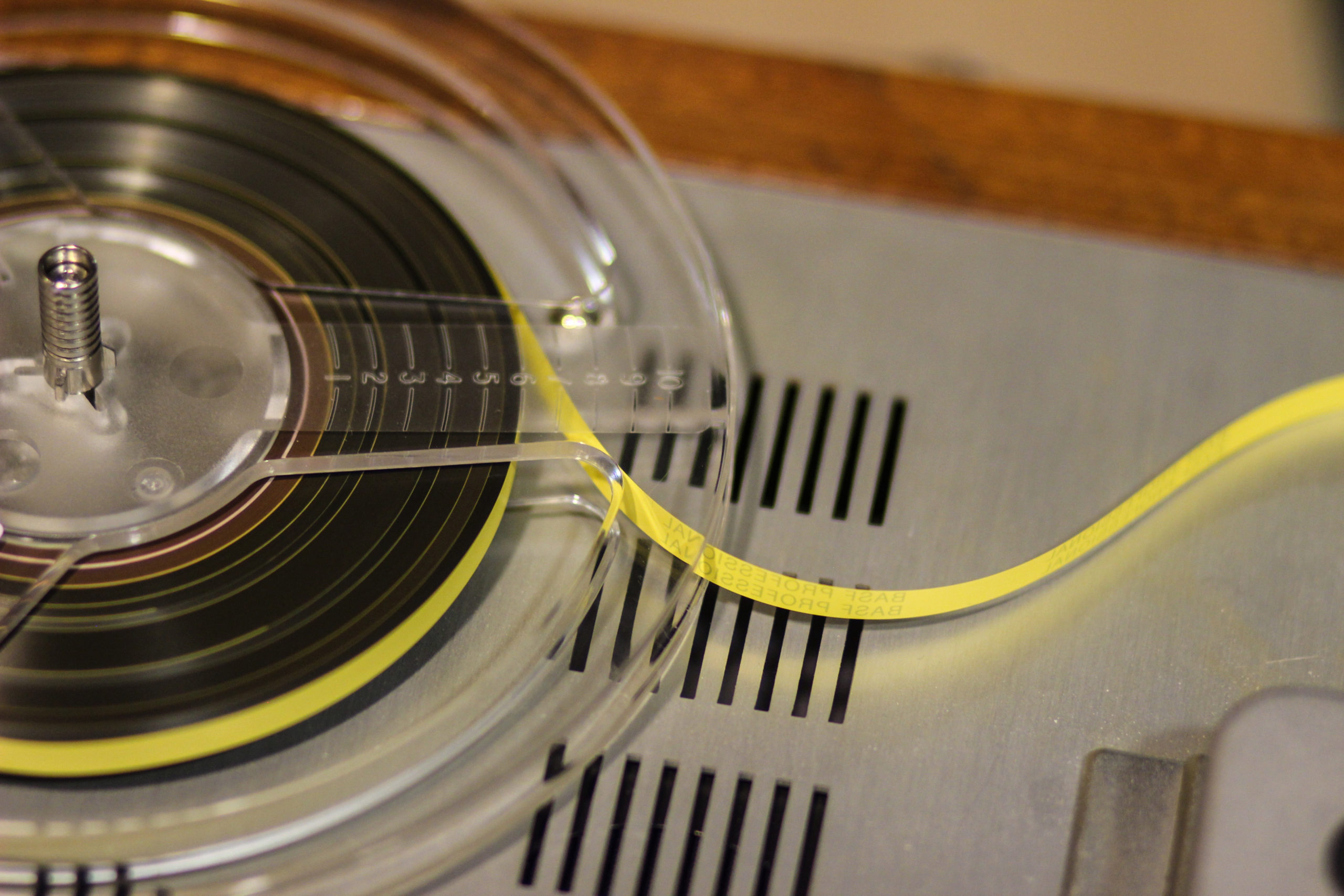 Photo of an open reel tape with tape, with tape spooling off to the right hand side, laying on the surface of a tape player.