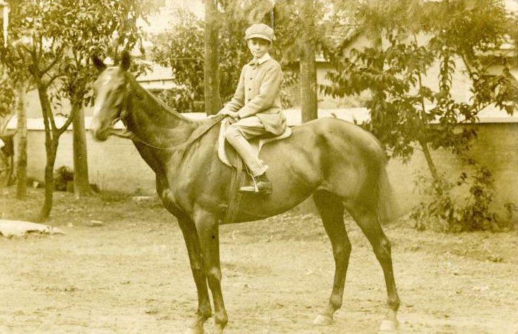 Black and white photo of Clifford George Burns as a boy, posing on horseback in the grounds of the family house in India, 1917