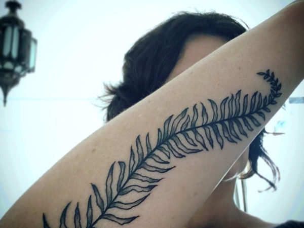 Lady holding up her arm to show a fern a black fern tattoo that runs up her forearm