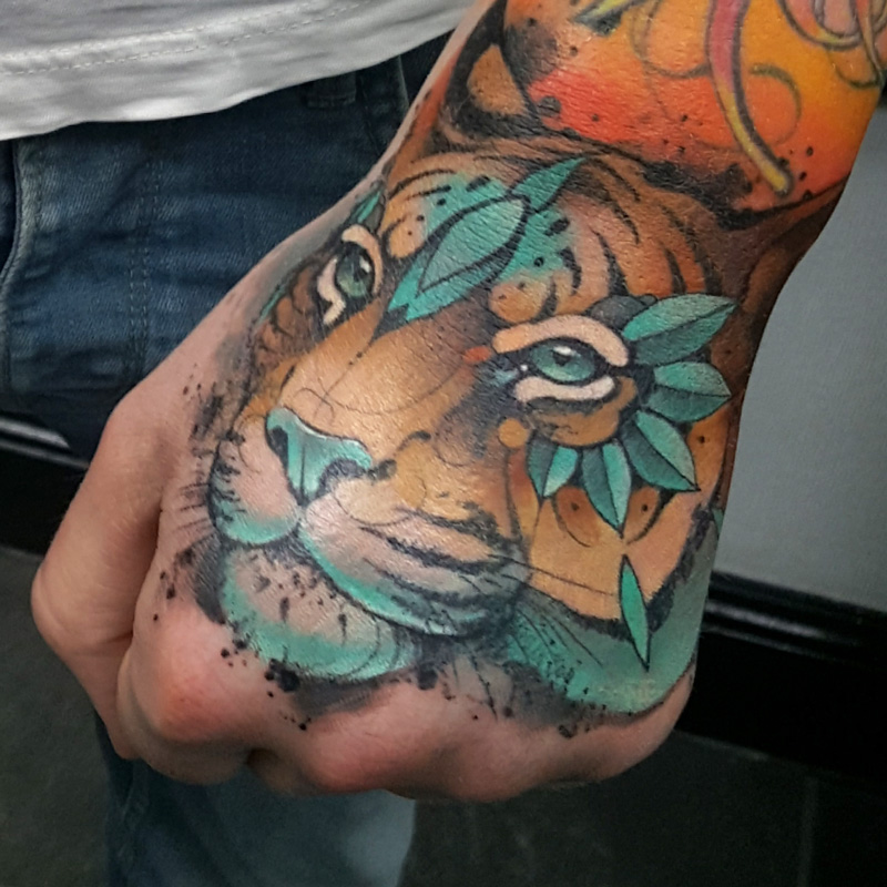 A tiger tattoo on a mans hand, it has bright blue embellishments on its forehead, eyes and mouth
