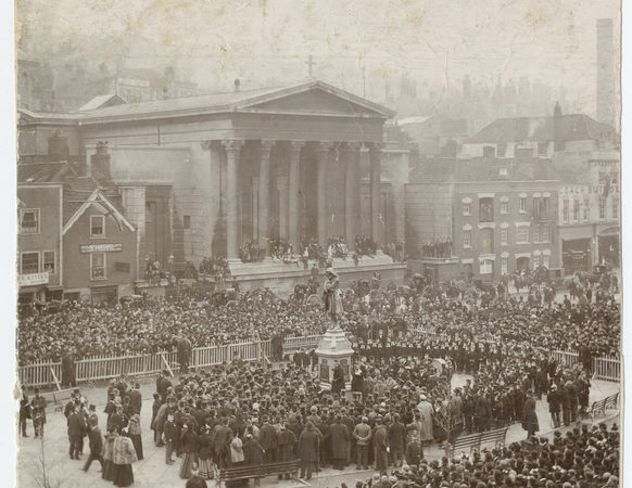 Sepia image of the opening ceremony of the statue of Colston. Large crowd of people surround the statue, with some areas barriered off.