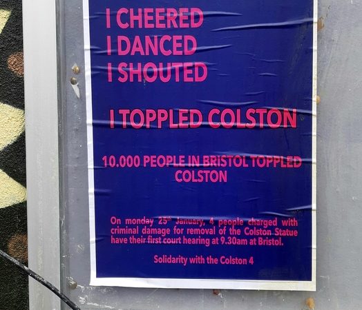 Blue poster with bright pink writing, on a noticeboard, behind cracked glass. ‘I CHEERED/ I DANCED/ I SHOUTED/ I TOPPLED COLSTON’/ 10,000 PEOPLE IN BRISTOL TOPPLED COLSTON/ On Monday 25th January, 4 people charged with criminal damage for removal of the Colston Statue have their first court hearing at 9.30am at Bristol./ Solidarity with the Colston 4’.